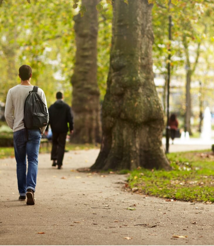 A man with a ruck sack walks through a leafy park